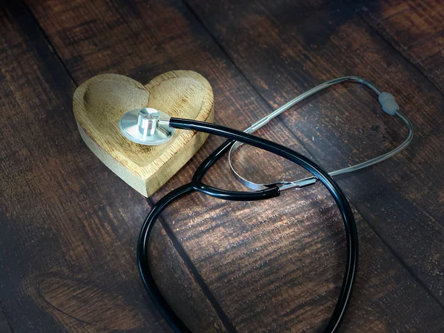 A doctor's stethoscope and a small wooden heart lying on a wooden surface.