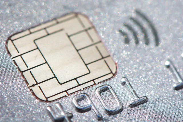 Macro photograph of a metallic credit-card chip and contactless-payment symbol.