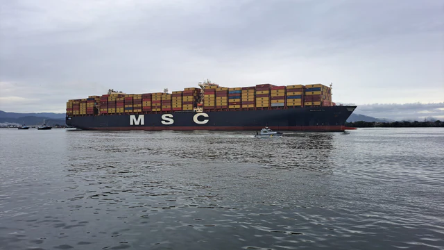A large container ship docked at the Port of Santos in Brazil, viewed across the harbor.