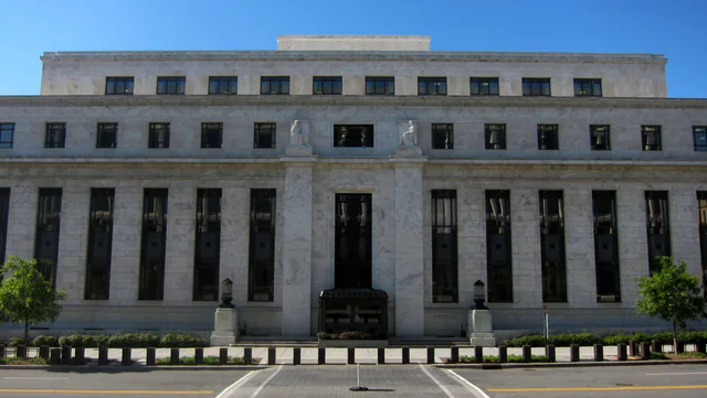 The stone north facade of the Marriner S. Eccles Federal Reserve Board Building in Washington, D.C., under a clear sky.