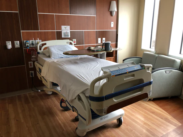 An empty modern hospital bed beside medical equipment in a private patient room.
