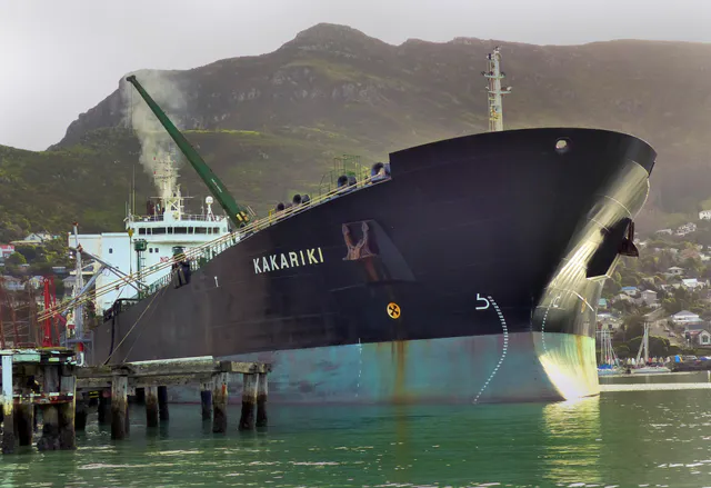 A large crude oil tanker ship floating on calm water under a clear sky, viewed from shore.