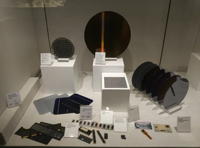 Several round, mirror-finish silicon semiconductor wafers stacked and fanned out, their surfaces reflecting rainbow-colored light.