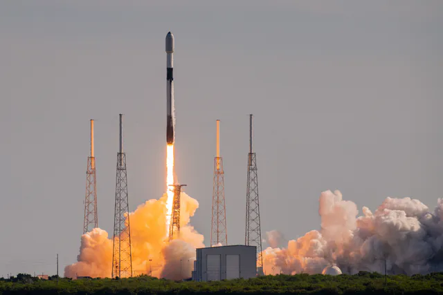 A SpaceX Falcon 9 rocket carrying Starlink satellites climbs into a blue sky on a column of flame and exhaust after lifting off from its launch pad at Cape Canaveral.