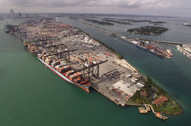Aerial photograph of a busy container terminal at the Port of Miami, with thousands of stacked shipping containers, gantry cranes, and cargo ships at the docks.