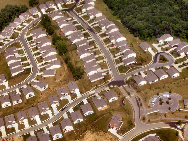 A row of similar two-story single-family suburban houses lining a quiet residential street under a clear sky.