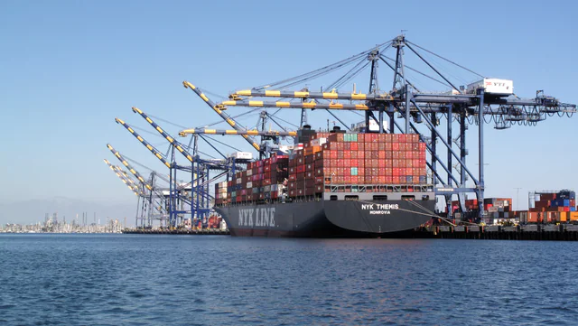 A large container ship stacked with intermodal shipping containers berthed beside gantry cranes at the Port of Los Angeles.