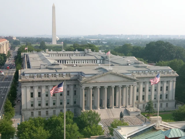 The neoclassical U.S. Treasury Building in Washington, viewed from the side with the Washington Monument in the background.