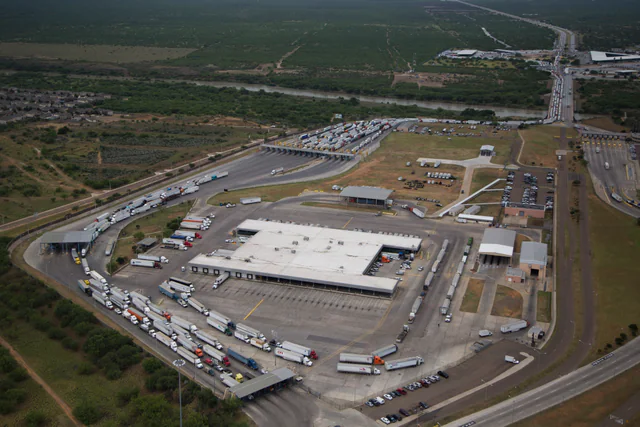 Long lines of tractor-trailer trucks queued on a multi-lane international bridge over the Rio Grande at a US-Mexico commercial border crossing.