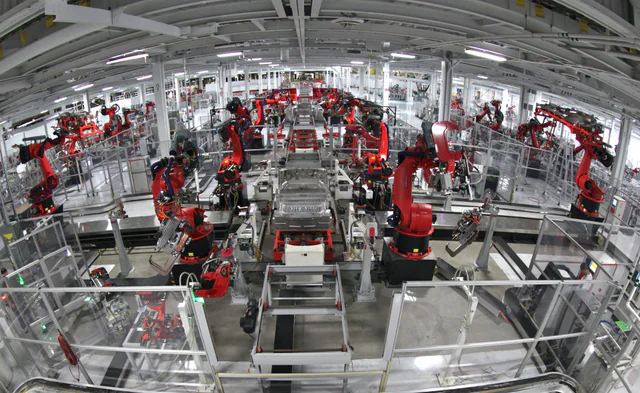 Robotic arms and conveyor stations along an automobile assembly line inside a large US factory floor.