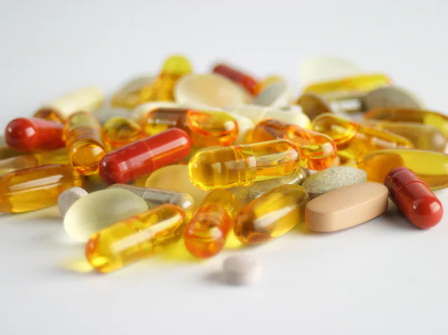 A pile of assorted oral capsules and tablets in red, amber and white on a plain background.